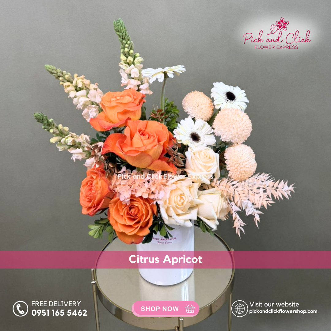 Citrus Apricot vase arrangement featuring orange and peach roses, white gerberas, orange sprayed pompons, snapdragons, dried ruscus, hydra, and sinamomo styled in a modern vase.
