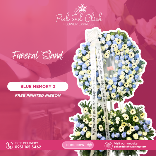 Blue Memory 2 funeral stand featuring white gerberas, imported white roses, white lisianthus, light blue-sprayed wonder white, rosal, anahaw, and selloum leaves in an elegant sympathy arrangement.