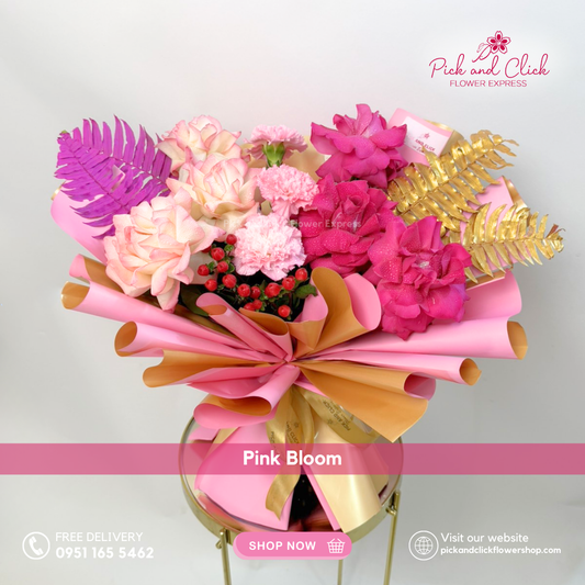 Pink Bloom bouquet featuring fuchsia pink roses, two tone pink roses, light pink carnations, berries, and pink and gold sprayed pako leaves arranged in a vibrant modern hand bouquet.